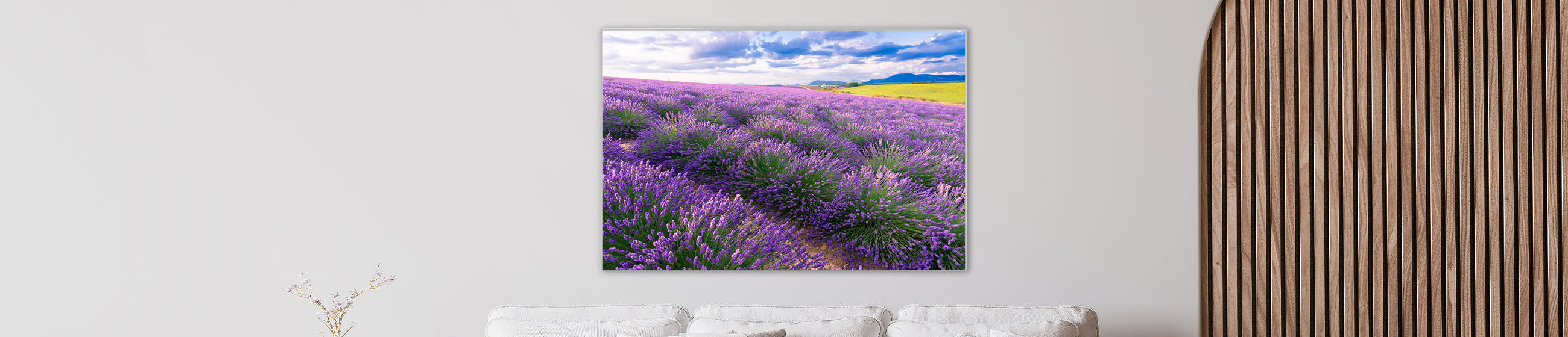 Fotokunst mit einem weiten Lavendelfeld in sattem Violett unter blauem Himmel mit Wolken, aufgehängt in einem modernen Wohnzimmer mit weißem Sofa.